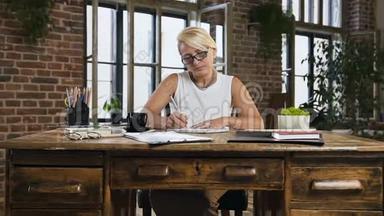 漂亮忙碌的女商人正在写日记，喝着咖啡坐在办公室的桌子<strong>后面</strong>