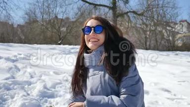 穿着蓝色镜子太阳镜和黑色<strong>直发</strong>的漂亮女孩在户外玩雪球。