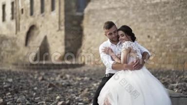 在城堡附近的石岸上观看充满爱的时尚新娘和新郎的户外照片。 行动。 漂亮的婚礼情侣