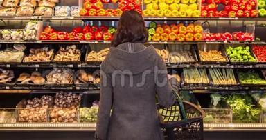 一个年轻的黑发女人站在杂货店一排农产品前面的移动框架。