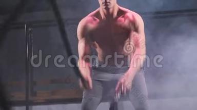 英俊的肌肉裸胸健身房男子与战绳在健身健身房锻炼。