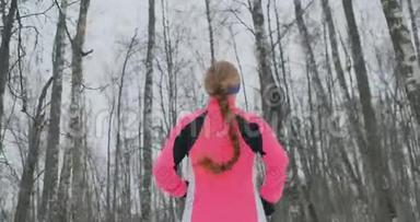 冬天，一个年轻的女人穿着一件粉红色的夹克穿过公园。 从后面看