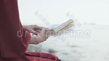 穿着红色衣服的女孩后面的景色在海边看书。 双手特写