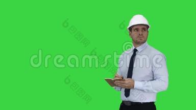 戴着头盔和正式衣服的男人四处<strong>走动</strong>，在绿色屏幕上做笔记，铬键。