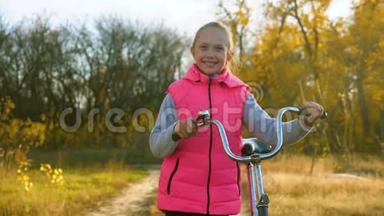 小女孩走在路上，把自行车<strong>卷起</strong>来。 秋天，孩子们在公园里散步。 快乐的女孩在镜头前挥手。 这就是