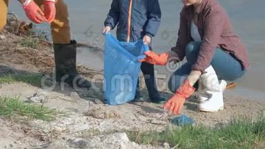 塑料污染，男人和女人带着小男孩戴着橡胶手套，在清理肮脏的海滩时，在垃圾袋里收集垃圾