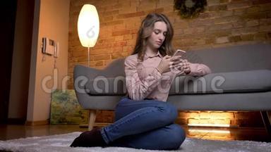 年轻女学生坐在地板上看手机和在舒适的家中情绪反应的画像
