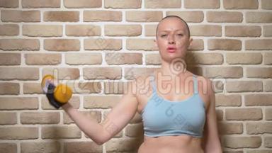 一个秃头女人在砖墙背景上用哑铃弯着胳膊。复制空间
