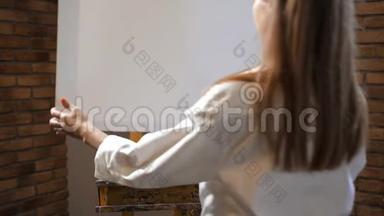 一个年轻的女人在画架上放一张画画布。 艺术工作室。 4K慢慢