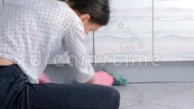 穿着粉红色橡胶手套<strong>的女人</strong>用布洗硬厨房家具。 <strong>坐在地板上</strong>。 后景。
