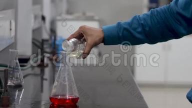 一位科学家把一种无色的化学物质从瓶子中倒入锥形瓶中的红色化学物质的手