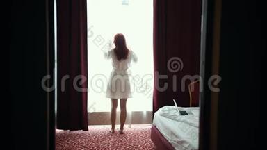 一个穿<strong>着</strong>浴袍的姜女打开酒店房间的窗帘，<strong>看着窗外</strong>