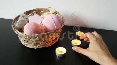 女人的手`长长地纠正了站在柳条箱旁边桌子上燃烧的蜡烛，上面放着用于洗澡的化妆品