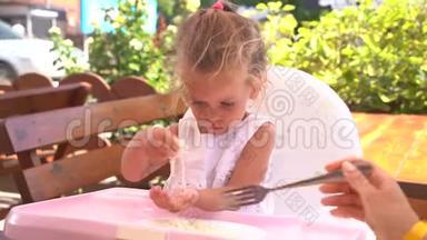 可爱的小白种人女孩在餐桌上吃意大利面，坐在儿童座椅户外餐厅。