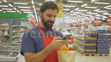 微笑<strong>超市</strong>员工使用手机，拿着购物袋在<strong>超市</strong>