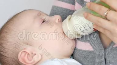 一个两个月的新生儿躺在母亲的手臂上，从一瓶牛奶中吸吮乳头。 4.这个孩子`了近景