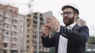 年轻的胡子建筑师在工地用平板电脑拍照。 他穿着商务服。