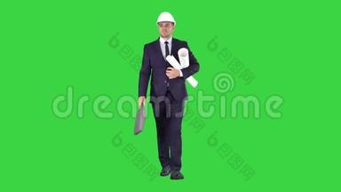 男建筑师穿着西装，戴着安全帽，带着蓝图和公文包走在绿色屏幕上，铬钥匙。