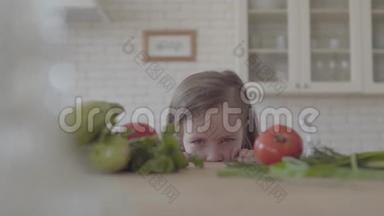 新鲜蔬菜西葫芦，西红柿和蔬菜放在桌子上。 那个可爱的小女孩从桌子上看，躲了起来