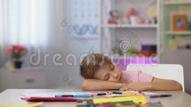 男学龄前儿童睡在桌子上，彩色铅笔和纸放在幼儿园桌子上