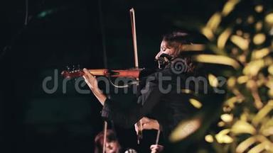 美丽的女孩小提琴手穿着黑色的衣服和长长的卷发在舞台上拉小提琴。 很酷的女<strong>音乐</strong>家。 慢节奏
