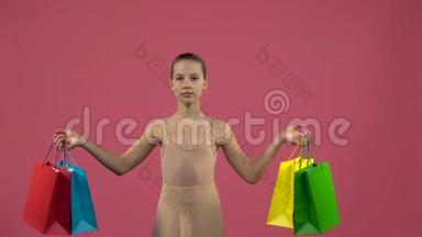 身着服装的儿童舞蹈演员带着购物袋在现场蹦蹦跳跳。 粉色背景。 慢动作