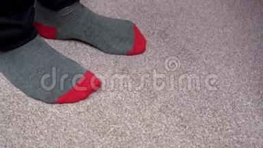 穿着红灰色袜子的脚在浅棕色地毯上互相摩擦。 站立站立