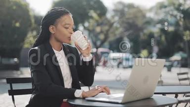 微笑的非裔美国女商人坐在<strong>夏日</strong>露台的<strong>咖啡</strong>馆里，喝着<strong>咖啡</strong>，在笔记本电脑上工作