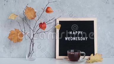 黑色信笺板上的“快乐星期三”文字，桌上花瓶里的衣柜上有一束黄叶子的树枝和一块石头