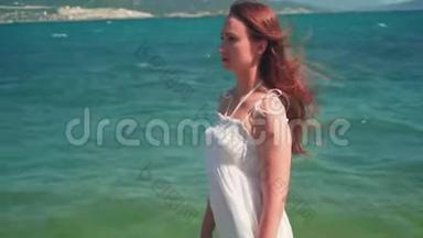 一个穿着白色海滩礼服的女孩，沿着海滨散步。 一个光着脚的漂亮女孩沿着海滨散步。