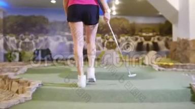 打<strong>迷你</strong>高尔夫。 一位年轻女子在室内打<strong>迷你</strong>高尔夫。 离球近一点，击中它，它就会进入洞里