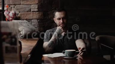一个男人坐在窗边，手臂上有纹身，在咖啡馆里写日记