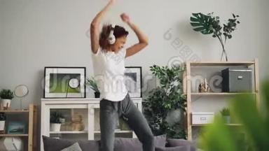美国一位有音乐感的非洲裔妇女正在家里的沙发上跳着舞，带着耳机听音乐，享受着节奏