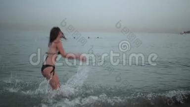 穿着黑色泳衣的年轻女孩在海滩上旋转，摆<strong>姿势拍照</strong>