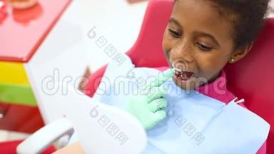 <strong>儿童</strong>`牙医在一张<strong>红色</strong>和黄色的牙科椅上检查一个可爱的非裔美国女孩的牙齿。