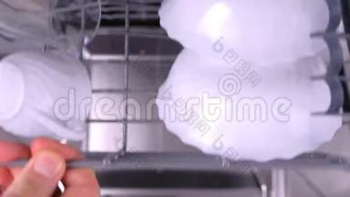 男人`手把脏盘子放进洗碗机里，用厨房用具推托盘。