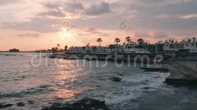 码头的粉色日落。 日落时美丽的行人区。 带棕榈的旅游长廊。 巨大的海浪在太阳下撞击码头