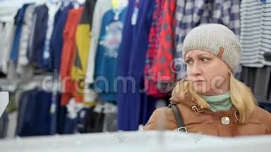 一个穿着冬衣戴着帽子的中年妇女去了一家儿童`<strong>服装</strong>店。 在<strong>货架</strong>上