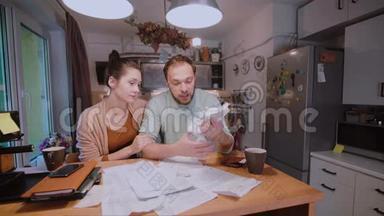 年轻夫妇在家里的厨房里计算账单。 女人试图平静悲伤和愤怒的丈夫。