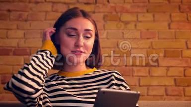 特写照片上年轻漂亮的女孩在平板电脑上打了一个视频电话，坐在平板电脑上愉快地笑着说话