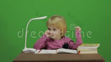 女孩坐在桌子旁，抠鼻子！ 课堂中的教育过程.. 快乐的三岁女孩。 可爱的女孩