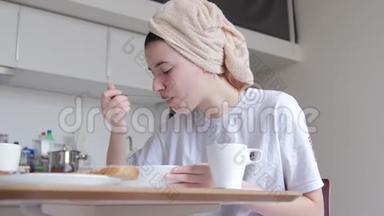一个头上戴<strong>着</strong>毛巾的年轻女孩正在吃早餐，吃早麦片，洗完澡，<strong>看着窗外</strong>
