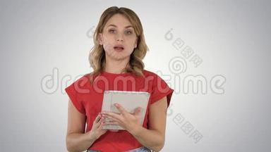穿着<strong>红色</strong>t恤的女士手里拿着一块平板电脑，严肃的脸在<strong>渐变</strong>背景上和相机交谈。