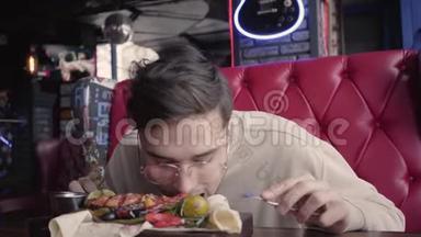 戴眼镜的英<strong>俊男</strong>子在不使用餐具的情况下吃他的食物。 满意的顾客吃烤鱼
