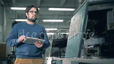 一个带着平板电脑的人正在检查一台运转良好的印刷设备