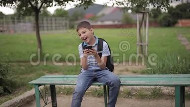 小男孩背着背包坐在长凳上，课间玩网络游戏