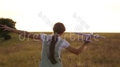 年轻女孩带着一架玩具飞机在田野上奔跑，在阳光下。 孩子们玩玩具飞机。 少年梦想