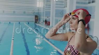 特写万向节拍摄。 自信的女游泳运动员正准备去游泳池游泳，戴上护目镜准备下水