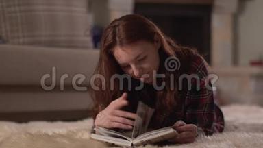 漂亮的年轻女人，穿着格子衬衫，躺在蓬松的地毯上，近距离阅读这本书。 女士<strong>翻页</strong>微笑