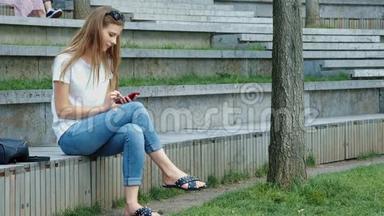 一个公园里年轻漂亮的女孩手里拿着一部智能手机，写着一条信息。 在电话里<strong>翻</strong>出<strong>照片</strong>